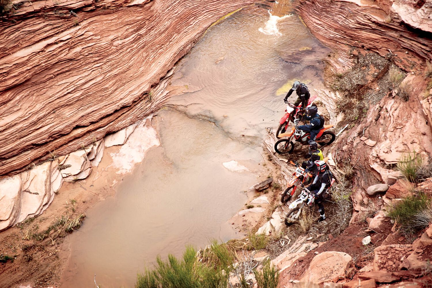 A group of enduro riders navigating a rocky stream.